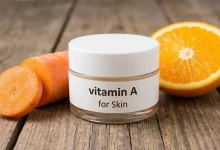 Luxury vitamin A retinol serum flat-lay with amber dropper bottle, golden oil droplets, raw carrot pieces, dried rose petals and capsules on soft beige background – skinguides.online